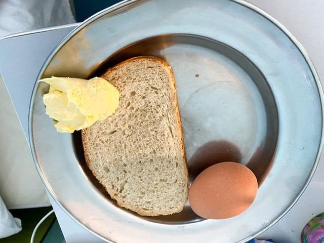 A plate with a slice of bread, a pat of butter, and a hard-boiled egg