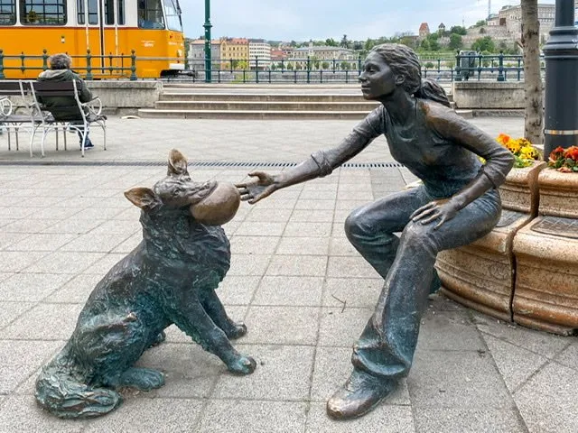 Statue of a girl reaching for a ball in a dog’s mouth