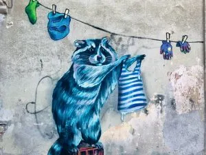 Mural of a blue raccoon hanging up laundry