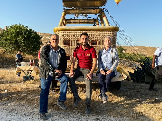 Three people sitting in front of a hot air balloon basket