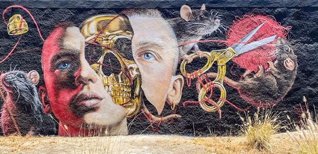 A mural with a boy’s head, a gold skull, scissors, yarn, and rats