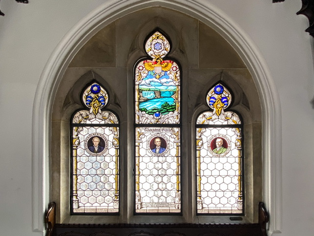 A stained glass window with Niagara Falls and three American men
