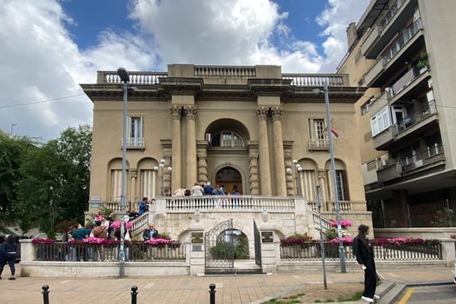 A tan building with people lined up on the staircase