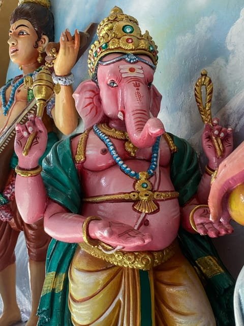 A statue of a pink elephant with four arms and embellishments