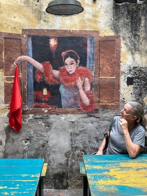 A mural of a woman waving a scarf out of a window and a real woman looking at her