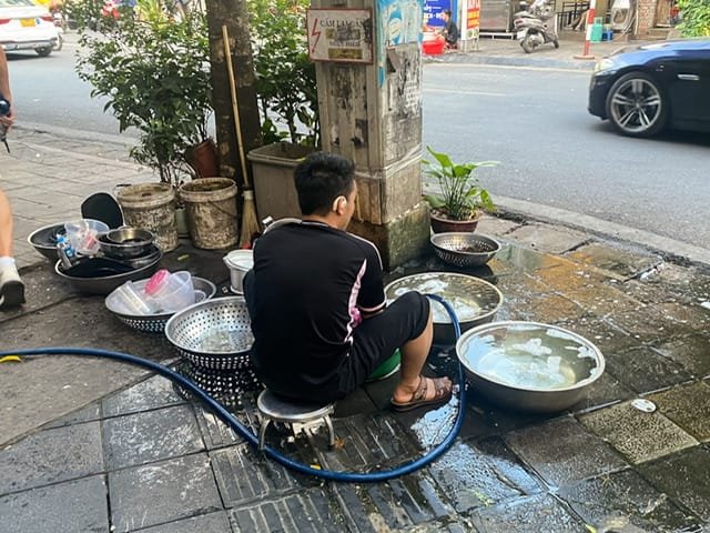 A man washing dishes in tubs on a sidewalk