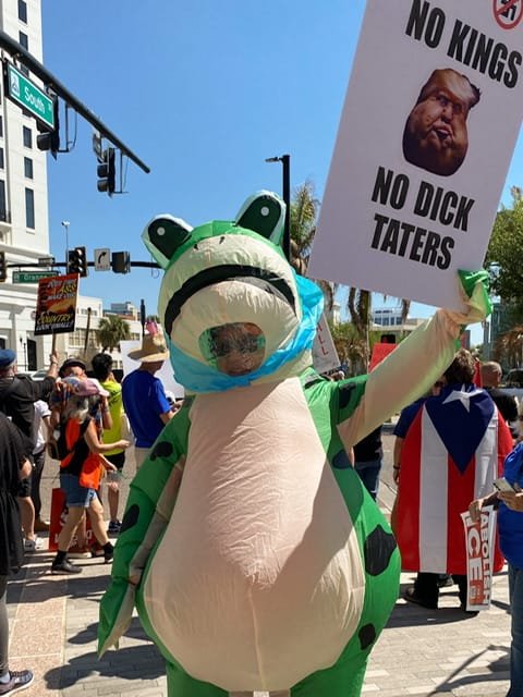 A person in a frog costume with a protest sign