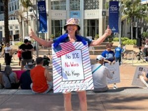 A woman with a protest sign and both thumbs up