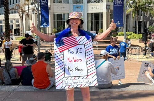 A woman with a protest sign and both thumbs up