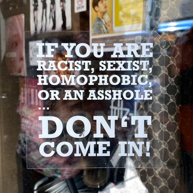A sign on a door reading “If you are racist, sexist, homophobic, or an asshole…don’t come in!”