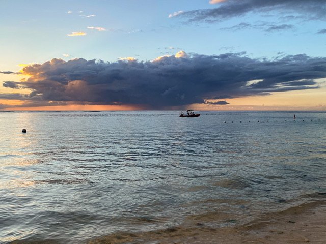 A large cloud over the ocean and a lone boat