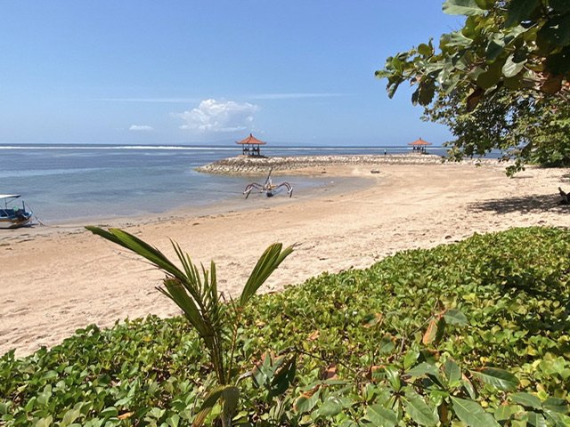 A beach with a pagoda, boats, trees, and vegetation